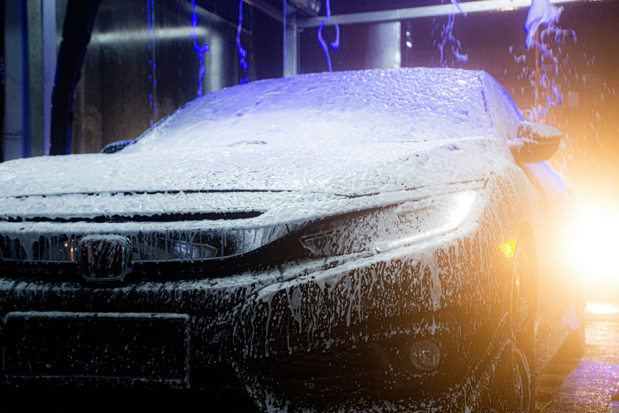 A car covered in thick foam inside the wash bay under dramatic lighting